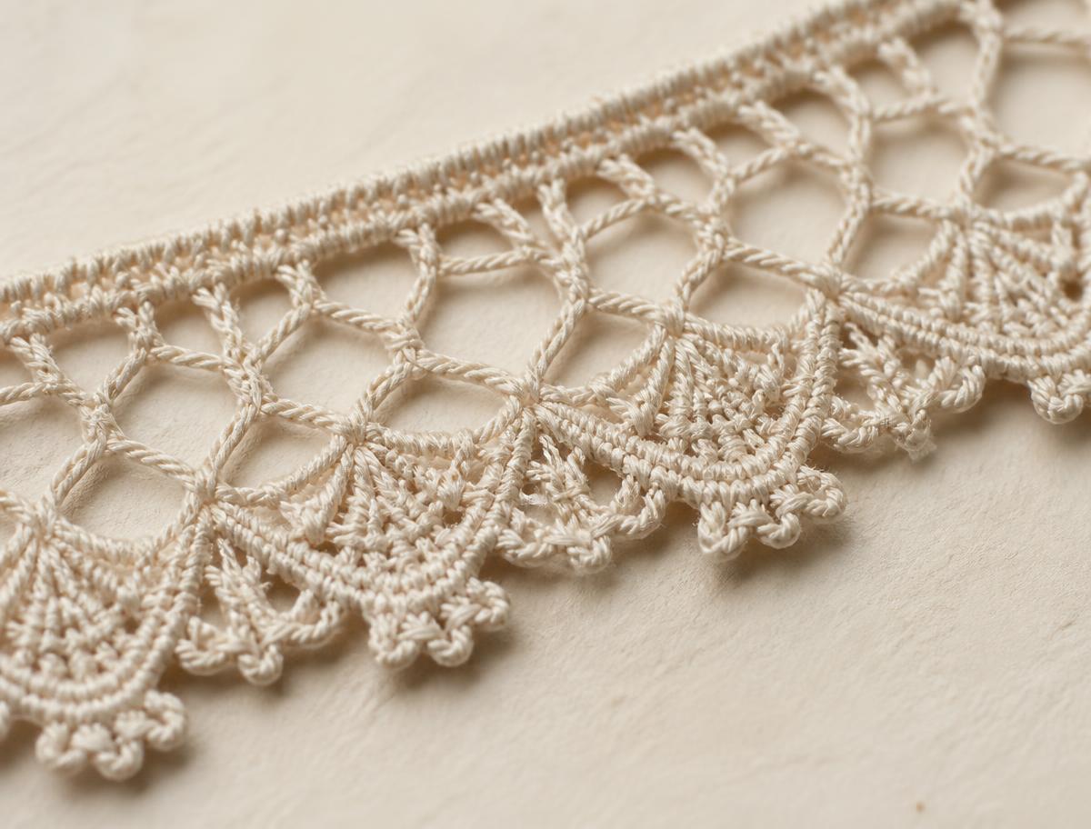 Close-up of a finished handmade bobbin lace edging in ecru linen thread